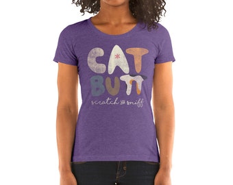 May include: Purple short-sleeved t-shirt with a graphic design of the words "CAT BUTT" in colorful, stylized letters. The text "scratch & sniff" is written in cursive below the graphic.
