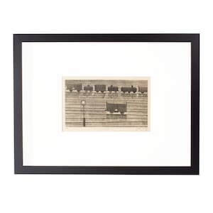 May include: Framed artwork featuring a sepia-toned print of train cars and a lamppost. The print is set against a white mat and enclosed in a black frame. The artwork evokes a vintage or industrial theme.