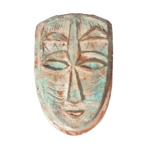 May include: A weathered, carved wooden mask with a serene expression. The mask features a symmetrical design with a prominent nose, almond-shaped eyes, and a slight smile. The color palette includes shades of turquoise, brown, and orange, giving it an aged appearance.