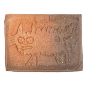 May include: A rectangular terracotta clay tile featuring an incised line drawing of a stylized creature with large circular eyes and a textured body. The word BULL is etched in the lower left corner. The tile has a gradient color finish.
