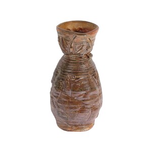 May include: A brown ceramic vase with a textured surface and a wide mouth. The vase has a unique design with raised lines and patterns.