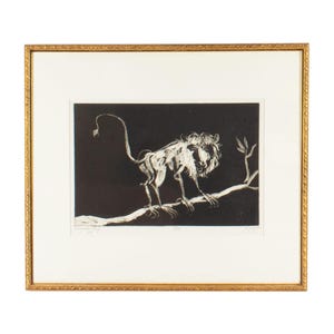 May include: A framed print featuring a black and white etching of a lion standing on a tree branch. The artwork is set against a solid black background, enclosed within a decorative gold-toned frame and a wide, off-white matting border.