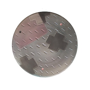 May include: A round ceramic plate with a geometric design in shades of gray, black, and pink. The plate has a textured surface and a hole in the center.