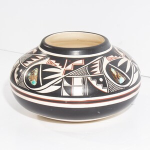 May include: A low-profile, rounded ceramic pot featuring a matte black finish with intricate white and terracotta geometric line patterns. The vessel is adorned with two inlaid, polished turquoise stones on opposite sides of the exterior surface.