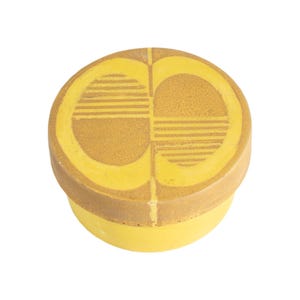 May include: A round ceramic container with a lid, featuring a bright yellow base and a lid with a textured, tan-colored geometric pattern consisting of two mirrored semi-circles, each divided into horizontal lines and a solid, grainy surface area.