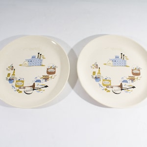 May include: Two white ceramic plates with a blue and gold design featuring a factory, musical instruments, and other objects. The plates have a white background with a gold rim.