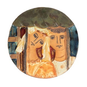 May include: A round ceramic plate with a painted scene of two people with their heads together. The plate has a blue, green, and brown glaze. The scene is signed "Ruth".