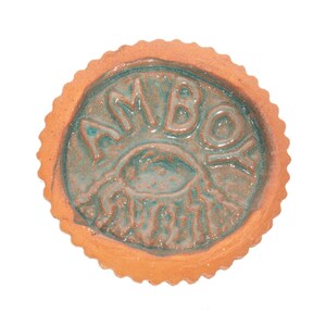May include: A round terracotta ceramic dish with a scalloped edge and a teal glazed center. The word AMBOY is embossed in a semi-circle above a central graphic of a stylized eye with radiating lines, all finished in a glossy teal glaze.