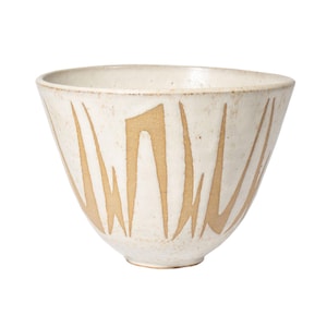 May include: Cream-colored ceramic bowl with a wide, open shape. The bowl features a series of vertical, abstract, tan-colored markings that create a textured pattern. The bowl's design is simple and modern, suitable for serving or display.