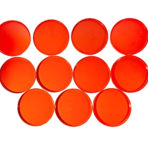 May include: Eleven bright orange, circular objects, possibly coasters or game pieces, are arranged against a white background. The objects have a glossy finish and a uniform size.