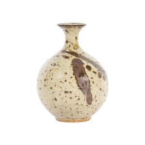 May include: A round ceramic vase with a narrow neck and flared rim. The surface is a speckled cream color with dark brown splatters and a prominent dark brown brushstroke pattern extending from the neck down the side of the spherical body.