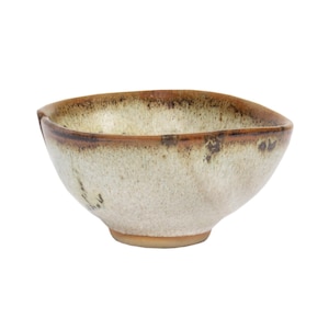 May include: A handmade ceramic bowl with a unique, asymmetrical shape. The bowl features a speckled, off-white glaze with a brown rim and base. The bowl is ideal for serving small portions of food.