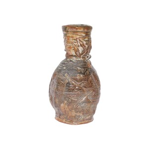 May include: A handcrafted ceramic vase with a textured surface and a unique, organic shape. The vase features a brown and gray color palette with embossed leaf and floral designs. The vase has a wide base and a narrow neck, making it a decorative piece.