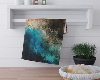 May include: A rectangular kitchen towel with an abstract design in shades of blue, brown, and beige hangs on a white shelf. The towel's design resembles a watercolor painting of ocean waves. A small potted plant and a basket of bread are in the foreground.