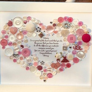 May include: A white frame with a heart-shaped design made of pink, white, and clear buttons. The heart is surrounded by a white background with a message that reads: "Valerie, I'm so proud of the hard work that you do, the person that you have become & all the difference you make for everyone around you. You are such a special person! Congratulations, Chrissy"