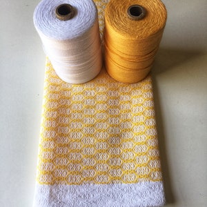 May include: Two spools of thread, one white and one yellow, are sitting on a yellow and white patterned fabric.