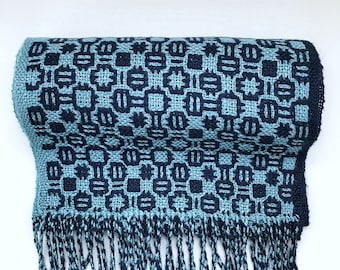 May include: A blue and black woven scarf with a geometric pattern and fringe on the bottom.
