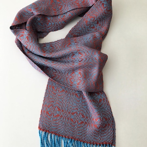 Könnte beinhalten: Ein blauer und roter gemusterter Schal mit Fransen. Der Schal ist aus einem weichen, gewebten Stoff.