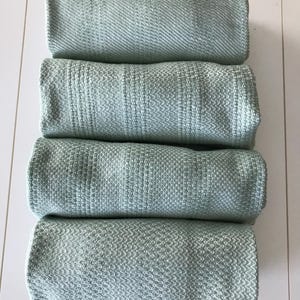 May include: Four folded light green cotton towels stacked on top of each other.