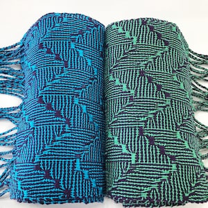 May include: Two woven scarves with a geometric pattern in shades of teal, green, and purple. The scarves have fringe on the ends.