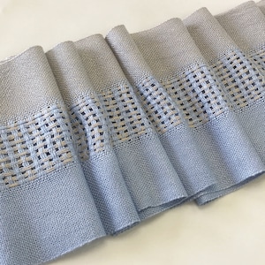 Puede incluir: Una cinta tejida de color azul claro y beige con un patrón geométrico. La cinta está doblada y tiene un aspecto suave y texturizado.