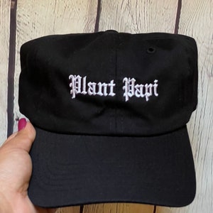 May include: Black baseball cap with a white embroidered inscription that reads "Plant Papi".