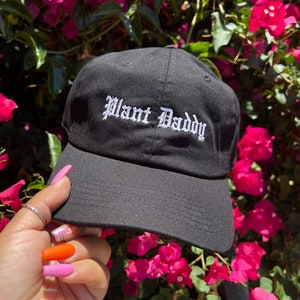 May include: Black baseball cap with white embroidered text that reads "Plant Daddy".