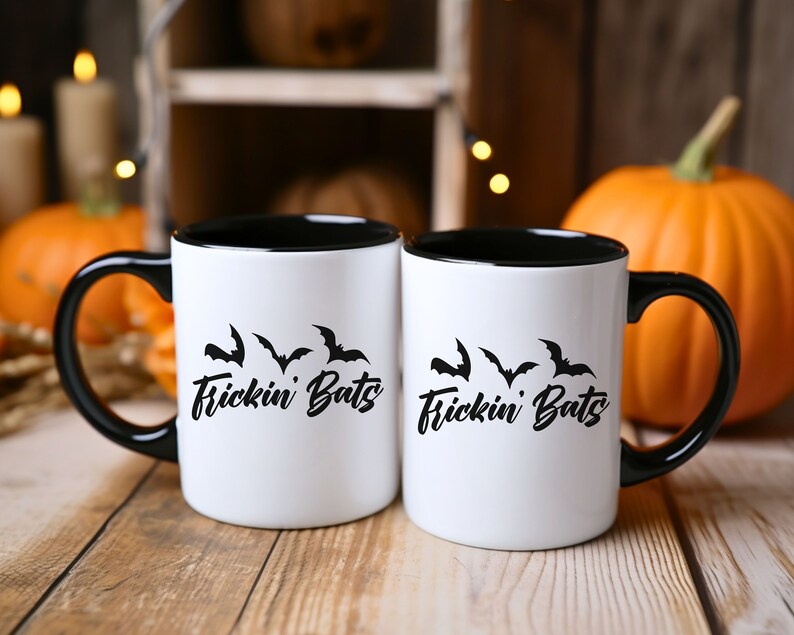 K&ouml;nnte beinhalten: Zwei wei&szlig;e Kaffeetassen mit schwarzen R&auml;ndern und Griffen. Die Tassen haben ein schwarzes Motiv mit Flederm&auml;usen und dem Text "Frickin' Bats" darauf.