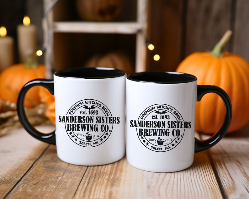 May include: Two white ceramic mugs with black handles and black rims. Both mugs feature a black and white logo that reads "Premium Witches Brew est. 1693 Sanderson Sisters Brewing Co. *** Salem, MA. ***"