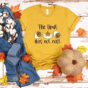 May include: Mustard yellow t-shirt with the text "The limit does not exist" and a graphic of deviled eggs. The shirt is surrounded by fall foliage and a decorative pumpkin.