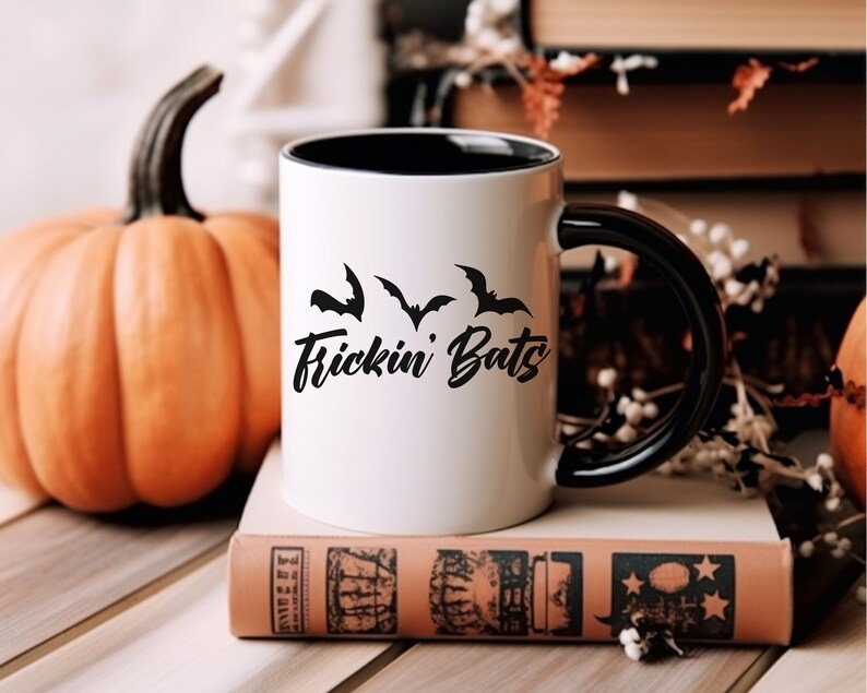 K&ouml;nnte beinhalten: Wei&szlig;e Keramiktasse mit schwarzem Rand und Henkel. Die Tasse hat ein schwarzes Motiv mit Flederm&auml;usen und dem Text "Frickin' Bats".