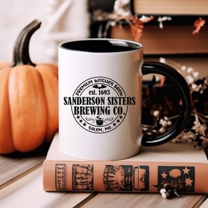 May include: White ceramic mug with a black handle and black rim. The mug features a black and white logo that reads "Premium Witches Brew est. 1693 Sanderson Sisters Brewing Co. Salem, MA."