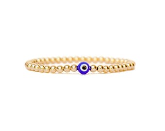 May include: A gold beaded bracelet with a blue evil eye charm.