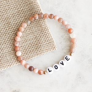 May include: A bracelet made of pink and brown beads with the word "LOVE" spelled out in white letters.