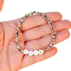 May include: A white and black speckled stone bracelet with gold accents and the word "LOVE" spelled out in white beads.