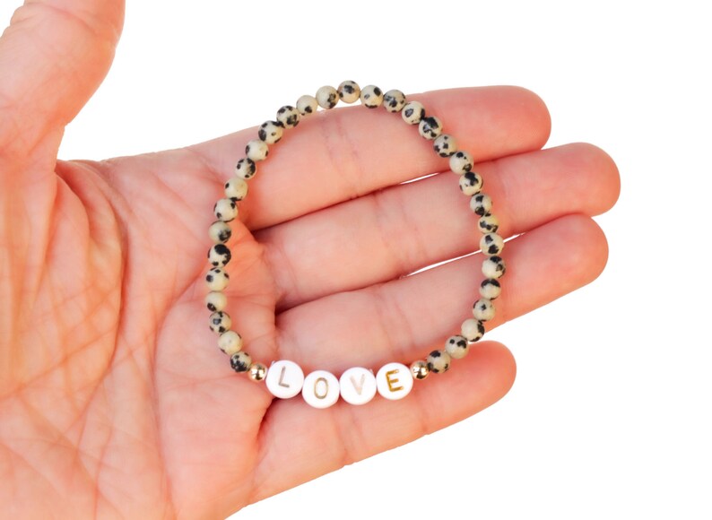 May include: A white and black speckled stone bracelet with gold accents and the word "LOVE" spelled out in white beads.