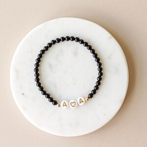 May include: A black beaded bracelet with gold letter beads spelling "A &hearts; A".