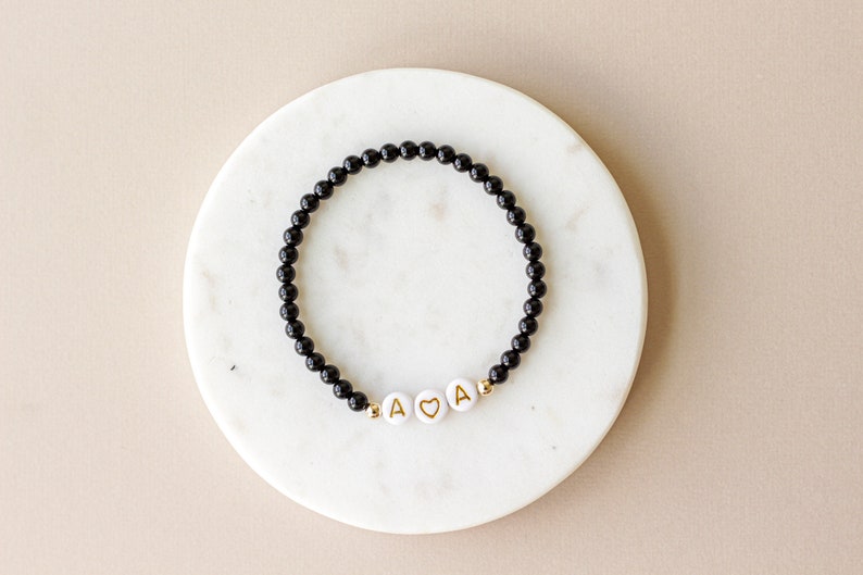 May include: A black beaded bracelet with gold letter beads spelling "A &hearts; A".