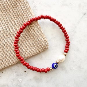 Peut inclure: Un bracelet circulaire compos&eacute; de petites perles rouge vif. Le design pr&eacute;sente une perle blanche nacr&eacute;e, une petite perle bleue et blanche en forme d'&oelig;il protecteur, et deux minuscules perles intercalaires m&eacute;talliques dor&eacute;es.