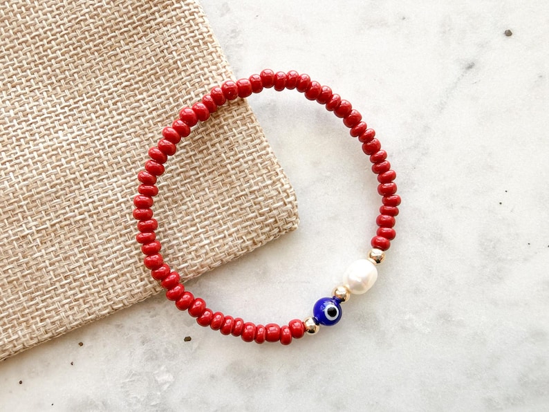 Peut inclure: Un bracelet circulaire compos&eacute; de petites perles rouge vif. Le design pr&eacute;sente une perle blanche nacr&eacute;e, une petite perle bleue et blanche en forme d'&oelig;il protecteur, et deux minuscules perles intercalaires m&eacute;talliques dor&eacute;es.