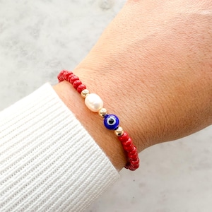 Peut inclure: Un bracelet de perles compos&eacute; de petites perles rouges sph&eacute;riques, d'une perle blanche ovale, d'une perle bleue et blanche en forme d'&oelig;il protecteur et de petites perles intercalaires m&eacute;talliques dor&eacute;es dispos&eacute;es en cercle.