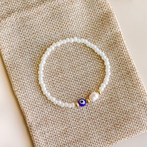 Peut inclure: Un bracelet de perles compos&eacute; de petites perles blanches translucides, d'une perle bleue et blanche en forme d'&oelig;il, d'une petite perle d'eau douce blanche et de deux minuscules perles intercalaires m&eacute;talliques dor&eacute;es.
