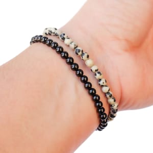 May include: Two bracelets on a wrist. One bracelet is made of black beads, the other is made of white and black speckled beads.
