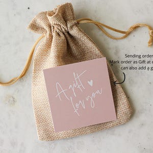 May include: A tan burlap drawstring pouch featuring a square pink card with the white text A gift for you and a small heart icon. An arrow points to the card with the text Sending order as a gift? Mark order as Gift at checkout and you can also add a gift message.