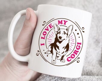 May include: White ceramic coffee mug featuring a brown and pink graphic of a corgi dog. The graphic reads "I love my corgi".