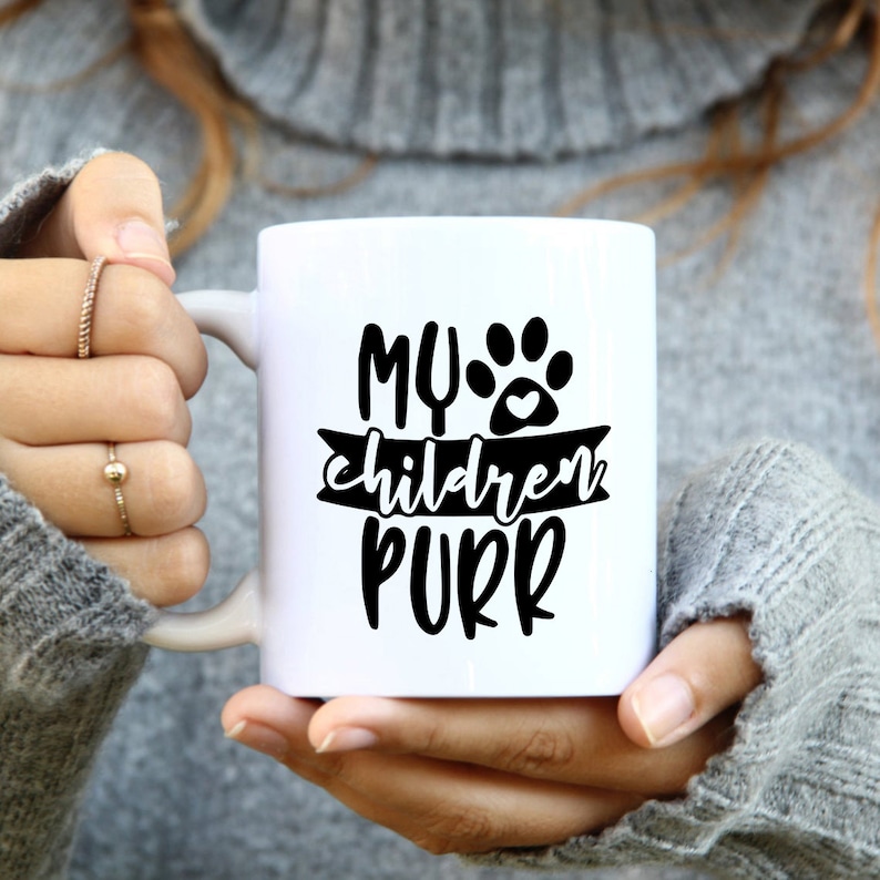 Może przedstawiać: Biały kubek ceramiczny z czarnym śladem łapy i tekstem "MY children PURR" na czarnym banerze.