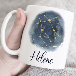 May include: White ceramic mug with a watercolor design of the Gemini constellation in gold. The name Helene is written in cursive below the constellation.