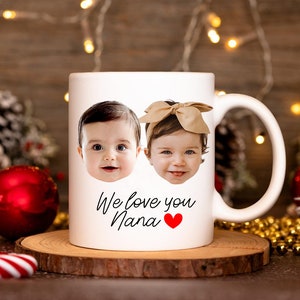 May include: White ceramic mug with two baby faces printed on it. The mug has the text "We love you Nana" with a red heart.