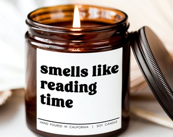 May include: A brown glass candle with a white label that reads "smells like reading time". The candle is lit and the lid is off. The label also says "Hand poured in California | Soy Candle".