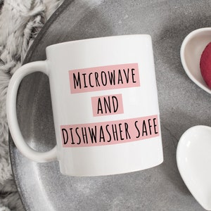 May include: White ceramic mug with black text that reads "Microwave and Dishwasher Safe" in pink rectangular boxes.